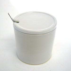 Può includere: Zuccheriera in ceramica bianca con coperchio e un piccolo cucchiaio.