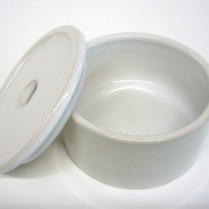 Könnte beinhalten: Weiße Keramikschüssel mit Deckel. Der Deckel hat ein kleines Loch in der Mitte.