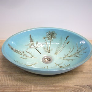 May include: A light blue oval ceramic sink with a drain and a design of pressed botanicals in gold.