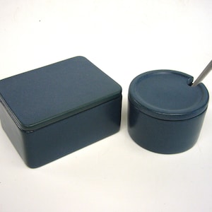Könnte beinhalten: Ein Set aus zwei blauen Keramikbehältern für Zucker und Sahne. Der Zuckerbehälter hat einen kleinen Löffel oben drauf.