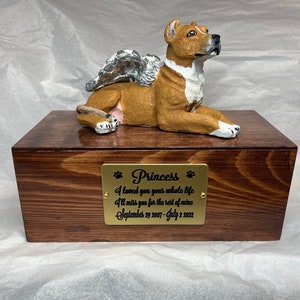 Può includere: Una scatola rettangolare in legno marrone scuro con una placca metallica dorata recante il testo Princess, I loved you your whole life, I'll miss you for the rest of mine, September 29 2007 - July 2 2022, sormontata da una statuetta di cane.