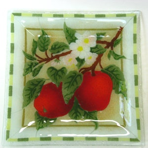 May include: Square glass dish with a green and white checkered border. The dish features a painted design of red apples on a branch with white blossoms and green leaves.