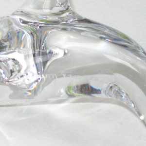 Op de afbeelding: Close-up van een helder, gebogen glazen object, mogelijk een decoratief stuk of onderdeel van een groter item. Het glas heeft een glad, reflecterend oppervlak met subtiele vervormingen en lichtbrekingen. Het object lijkt transparant te zijn, met een lichte kromming.