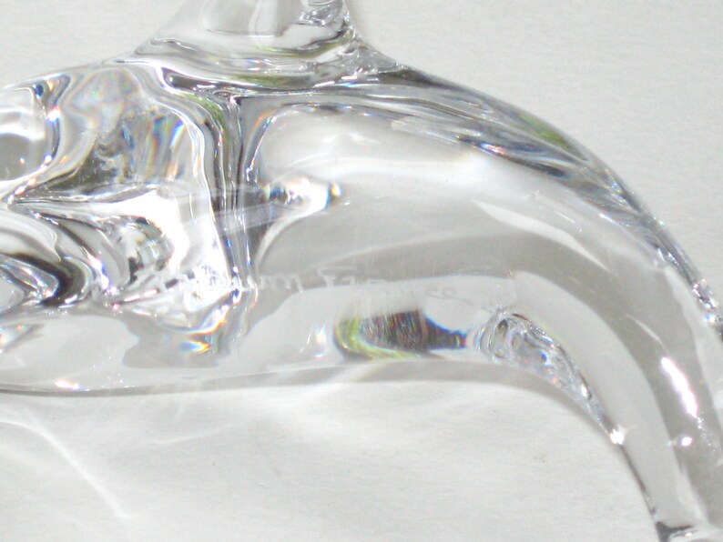 Op de afbeelding: Close-up van een helder, gebogen glazen object, mogelijk een decoratief stuk of onderdeel van een groter item. Het glas heeft een glad, reflecterend oppervlak met subtiele vervormingen en lichtbrekingen. Het object lijkt transparant te zijn, met een lichte kromming.