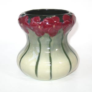 May include: A ceramic vase with a bulbous base and a flared rim. The vase is painted with a light green and cream color scheme, with vertical green stripes. The rim is adorned with red floral accents.