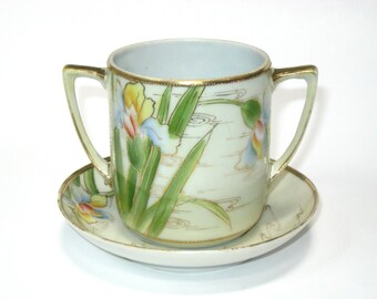 Taza y platillo Morimura Nippon con dos asas, porcelana con irises dorados pintados a mano; juego antiguo en amarillo y verde, con un movimiento estético.