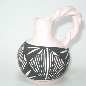 May include: A small, white ceramic pitcher with a black and white geometric design. The pitcher has a twisted handle and a rounded body.