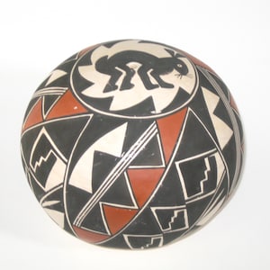 May include: A black and white pottery bowl with a red geometric design. The bowl features a black silhouette of a rabbit on the top.