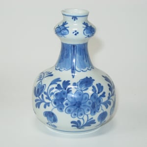 May include: A small, white ceramic vase with a blue and white floral design. The vase has a bulbous body and a narrow neck.