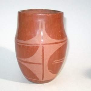 May include: A terracotta pottery vase with a geometric design in a lighter shade of terracotta. The vase is round and has a slightly flared lip.