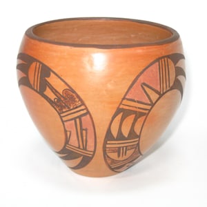 May include: A handmade, terracotta-colored pottery bowl with a wide opening and rounded sides. The bowl features symmetrical, hand-painted designs in shades of brown and orange. The designs include geometric shapes and stylized patterns.
