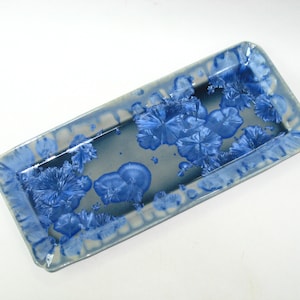 May include: Rectangular ceramic tray with a blue and gray glaze. The tray features a raised rim and is decorated with crystalline blue floral patterns. The tray is a decorative piece for serving or display.