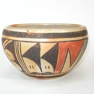May include: A small, round, ceramic bowl with a geometric design in black, brown, and red. The bowl is decorated with a pattern of triangles and lines.