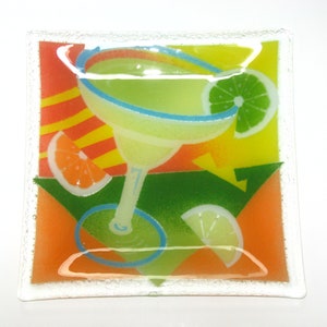 May include: A square glass serving dish with a colorful design featuring a margarita glass, lime wedges, and orange slices. The background is a mix of yellow, orange, and green.