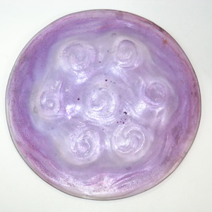 May include: A round, ceramic plate with a light purple glaze and a white center. The center has a design of five raised swirls.