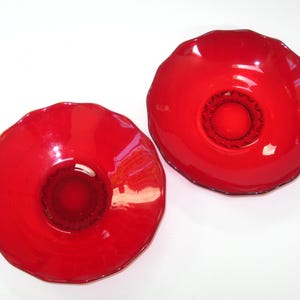 May include: Two vibrant red glass bowls with a ruffled edge. The bowls have a glossy finish and a circular design in the center. The bowls are placed on a white surface.