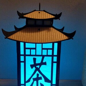 May include: A black wooden lantern with a blue light inside. The lantern has a traditional Chinese design with a pagoda roof and a lattice window. The word "茶" (tea) is cut out of the window.