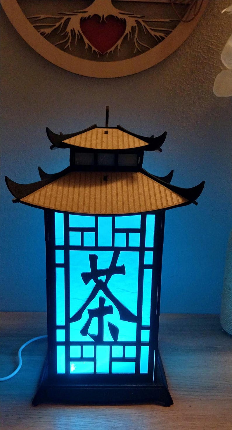 May include: A black wooden lantern with a blue light inside. The lantern has a traditional Chinese design with a pagoda roof and a lattice window. The word "茶" (tea) is cut out of the window.