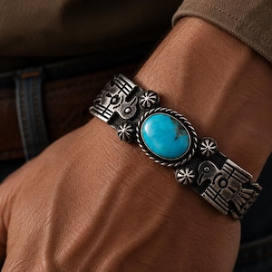May include: A silver cuff bracelet featuring a central oval turquoise stone with a rope-style border. The metal band is decorated with engraved bird motifs and small star-shaped accents, showcasing a dark oxidized finish in the recessed areas.