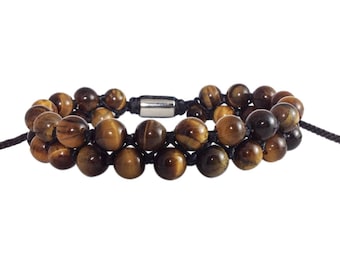 Puede incluir: Un brazalete de doble fila hecho con cuentas de ojo de tigre y cordón negro. El brazalete tiene un cierre plateado.