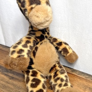 May include: A plush giraffe toy with a tan muzzle, brown spots, and brown hooves. The giraffe has small brown horns and is made of soft, fuzzy material. The toy is designed to resemble a giraffe.