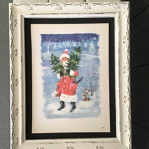 May include: A framed illustration of Father Christmas carrying a Christmas tree in a snowy winter scene. The illustration is in a white frame with a black mount.