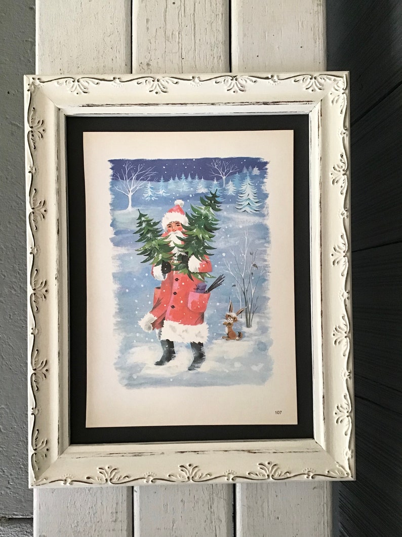 May include: A framed illustration of Father Christmas carrying a Christmas tree in a snowy winter scene. The illustration is in a white frame with a black mount.
