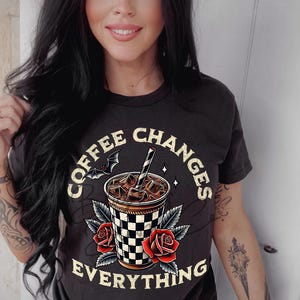 May include: A black t-shirt with a graphic of a coffee cup with ice and a bat. The text "Coffee Changes Everything" is printed on the shirt.