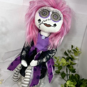 May include: A handmade rag doll with pink hair, a purple dress, and black lace trim. The doll has button eyes and a stitched mouth.