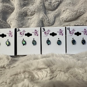 May include: Four pairs of iridescent green and blue oval-shaped earrings on white cards with butterfly designs. The cards are numbered 1 through 4.