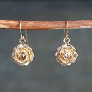 May include: A pair of gold-toned dangle earrings with a rose design. The earrings have a delicate, feminine look.