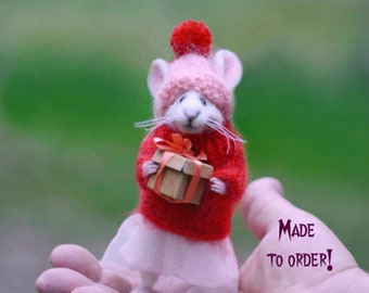 May include: A handmade miniature mouse figurine wearing a red sweater, pink hat, and white skirt, holding a small gift box. The mouse has white whiskers and is set against a blurred green background. The text "MADE TO ORDER!" is visible.