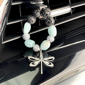 Könnte beinhalten: Ein Luftauslass-Diffusor mit einem Libellen-Anhänger. Der Diffusor hat schwarze Lavasteinperlen, hellblaue Edelsteinperlen und silberfarbene Strassakzente. Der Libellen-Anhänger ist silberfarben mit klaren Strassakzenten.