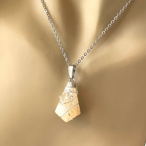 May include: A silver-toned necklace featuring a pendant with a light yellow, irregularly shaped stone. The stone is encased in a silver wire cage and hangs from a delicate chain. The pendant has a polished finish, and the chain is simple and elegant.