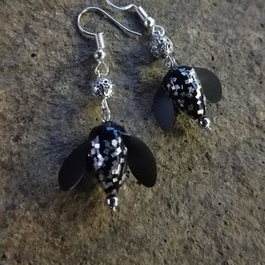 May include: A pair of silver dangle earrings with black and white glitter flower-shaped charms.