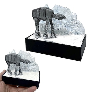 Könnte beinhalten: Eine graue AT-AT Star Wars Walker-Figur, die auf einem weißen Schneesockel mit einem weißen Eisberg im Hintergrund steht. Die Figur steht auf einem schwarzen rechteckigen Sockel.