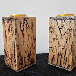 Puede incluir: Dos portavelas de madera con un acabado rústico de madera quemada. Cada portavelas tiene una pequeña vela redonda amarilla en la parte superior.