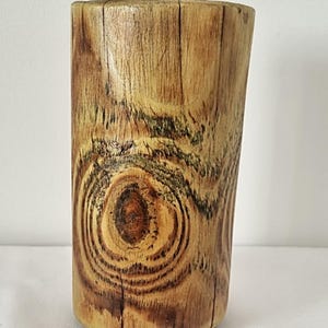 Può includere: Un portacandele in legno rustico con una finitura in legno naturale. Il portacandele ha una forma cilindrica e presenta un motivo circolare di venature del legno.