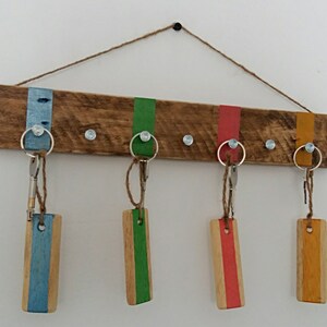Puede incluir: Porta llaves de madera con cinco ganchos, pintado con rayas azules, verdes, rojas y amarillas. El porta llaves está hecho de madera reciclada y tiene un aspecto rústico.