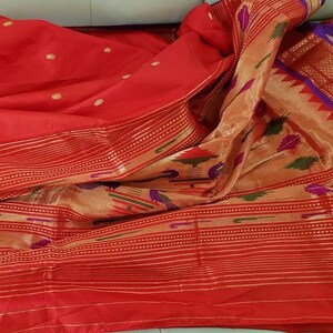 May include: A red and gold saree with a patterned border. The saree is made of silk and has a traditional Indian design.