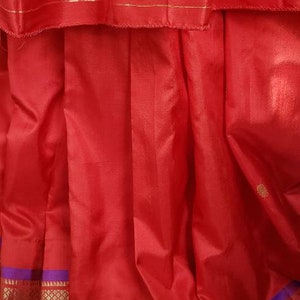 May include: Red silk saree with a purple and gold border. The saree has a traditional Indian design and is perfect for special occasions.