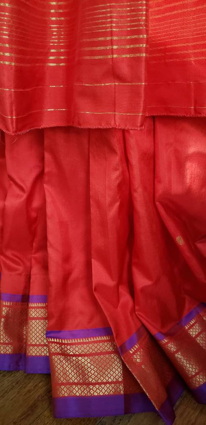 May include: Red silk saree with a purple and gold border. The saree has a traditional Indian design and is perfect for special occasions.