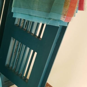 May include: A teal blue sheer fabric with a gold and orange trim. The fabric is draped over a teal blue wooden frame with a lattice design.