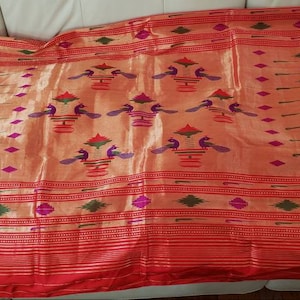 May include: A red and gold silk saree with a purple border and intricate peacock designs. The saree has a traditional Indian design with a woven pattern.