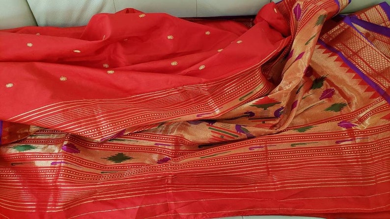 May include: A red and gold saree with a patterned border. The saree is made of silk and has a traditional Indian design.