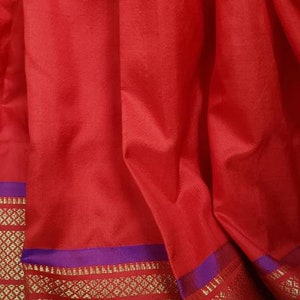 May include: Red fabric with a purple and gold border. The border has a repeating geometric pattern.