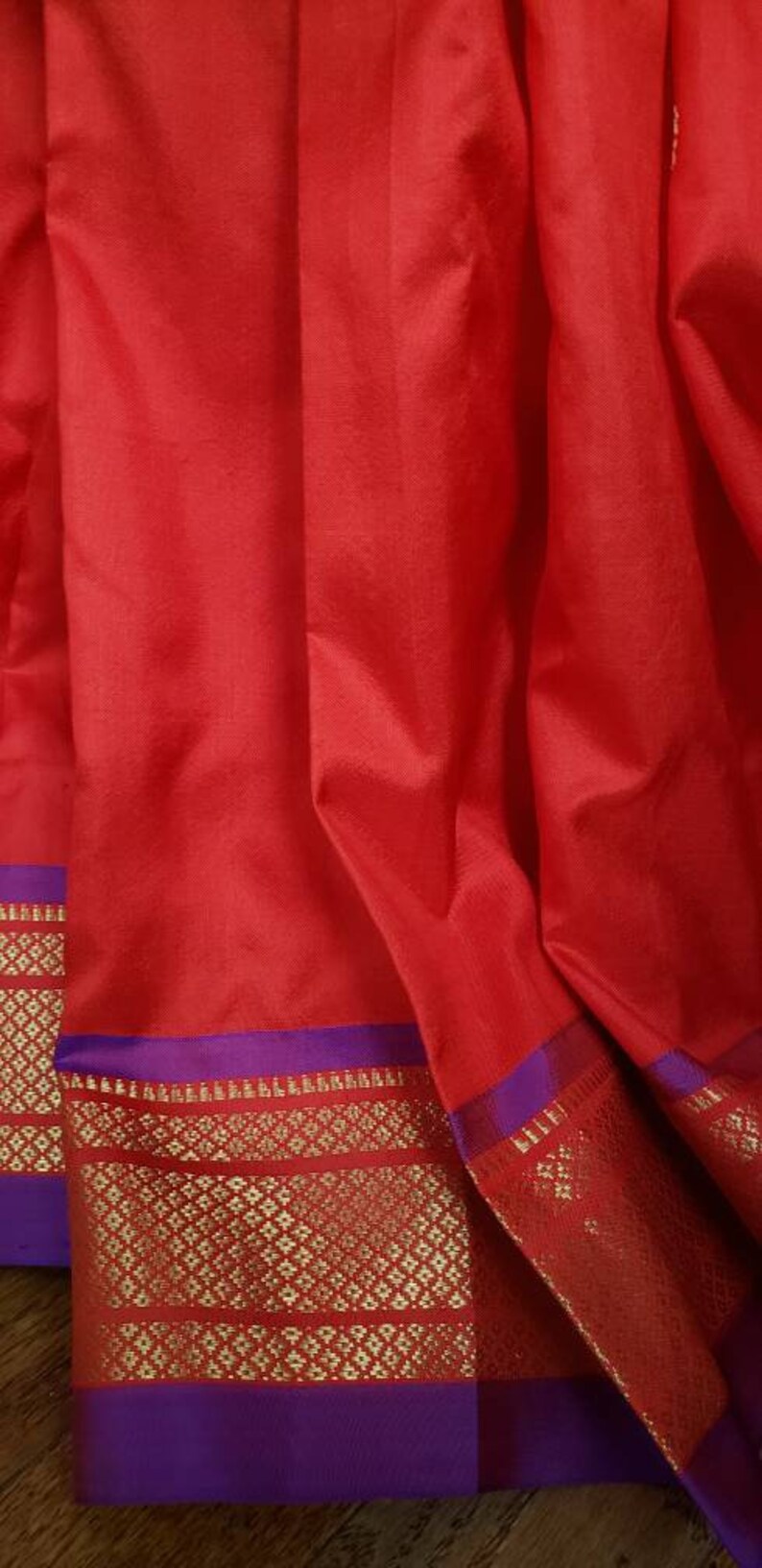 May include: Red fabric with a purple and gold border. The border has a repeating geometric pattern.