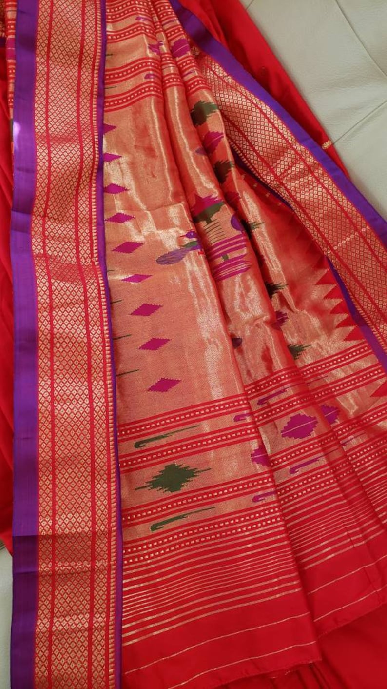 May include: A red and gold saree with a purple border and intricate woven patterns. The saree is made of silk and has a soft, luxurious feel.