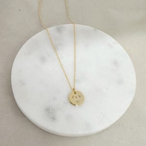 May include: A gold necklace with a round pendant that has the letters "ALS" engraved on it. The pendant is on a white marble surface.