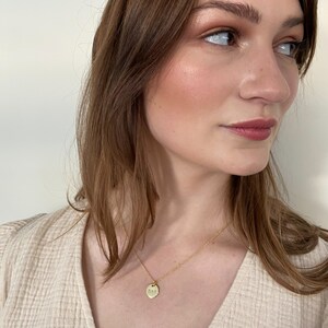 May include: A gold necklace with a small, round pendant. The pendant has a textured surface and is hanging on a delicate chain.